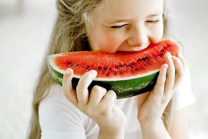 Petite fille en train de mordre dans une tranche de melon d'eau