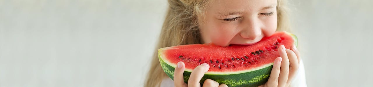 Small girl biting into a piece of watermelon