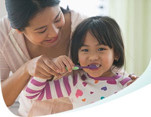 Mom helps her daughter brush her teeth with Pronamel® 