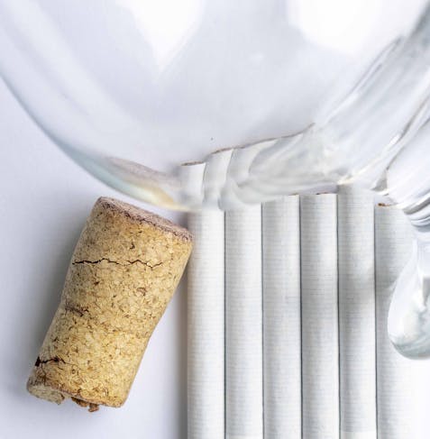 Wine cork lying on a table next to a glass and 6 cigarettes