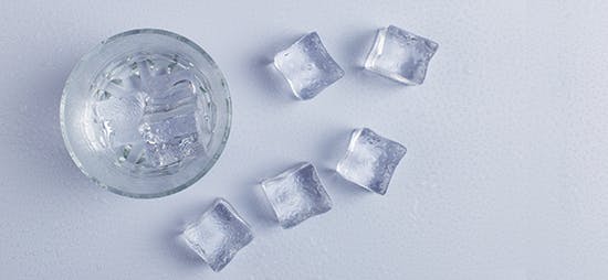Glass of water on a table surrounded by ice cubes