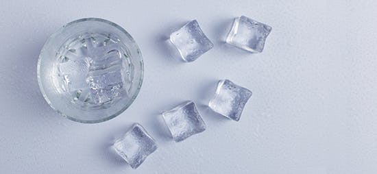 Glass of water on a table surrounded by ice cubes Glass of water on a table surrounded by ice cubes