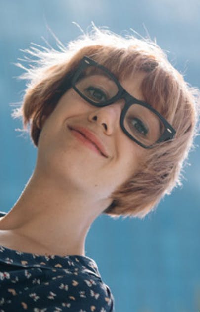 Woman wearing dark rimmed glasses and smiling with a blue sky background