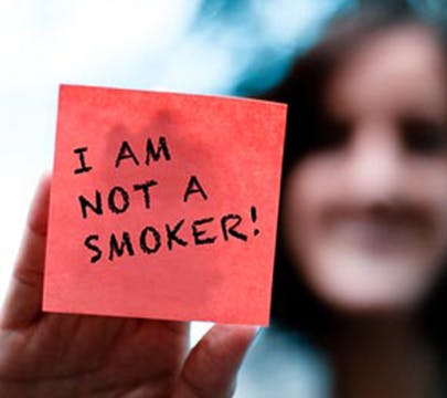 Woman holding a post-it note up to some glass that says “I AM NOT A SMOKER”