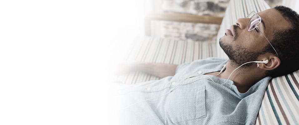 Man laying on a futon with his eyes closed, listening to headphones