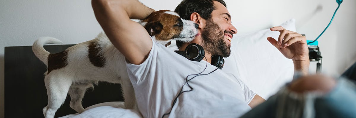 Un homme couché dans son lit, riant pendant que son chien le câline