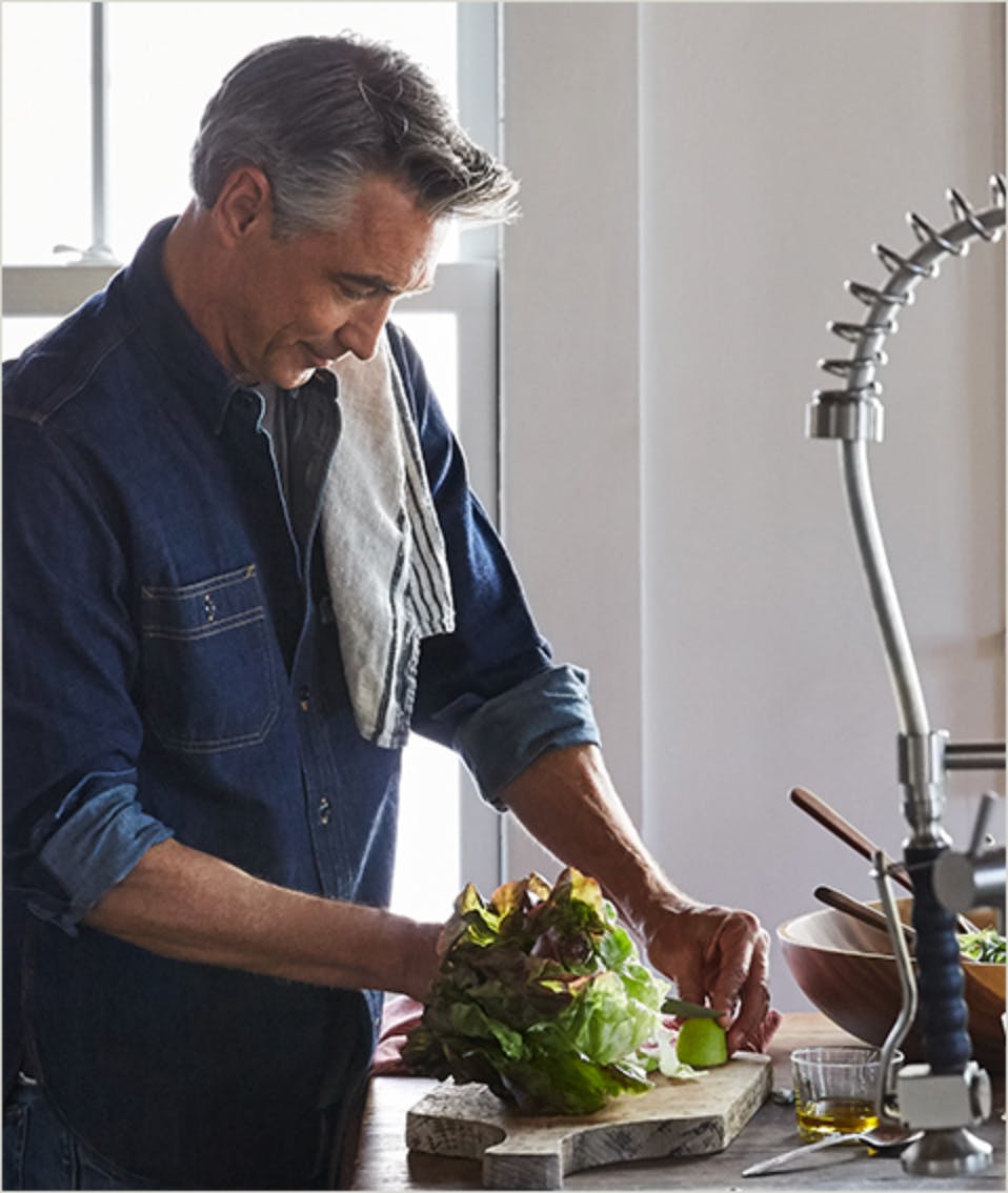 Un homme dans une cuisine découpant des légumes pour une salade