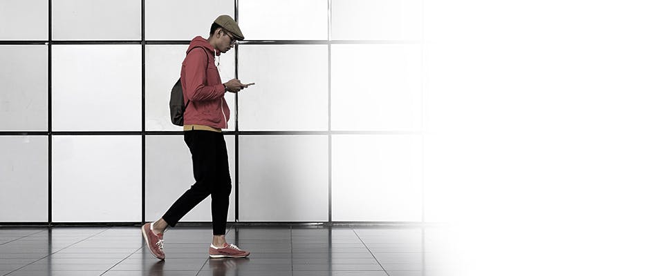 Un homme portant un chandail à capuchon rouge en train de marcher dehors avec un téléphone cellulaire