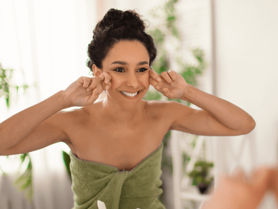 Smiling woman applying skincare at her sink 