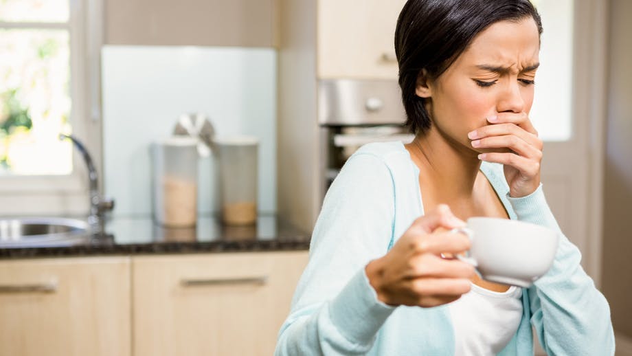 Woman in pain holding her mouth and a coffee cup