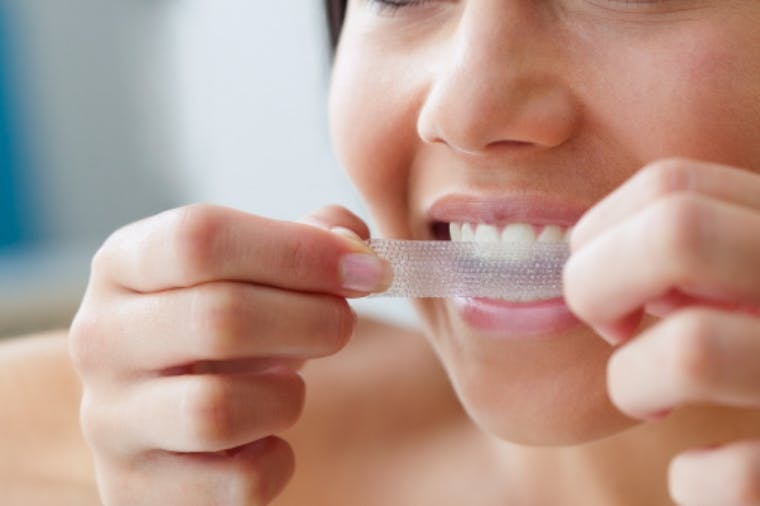 Woman using whitening strips on her sensitive teeth