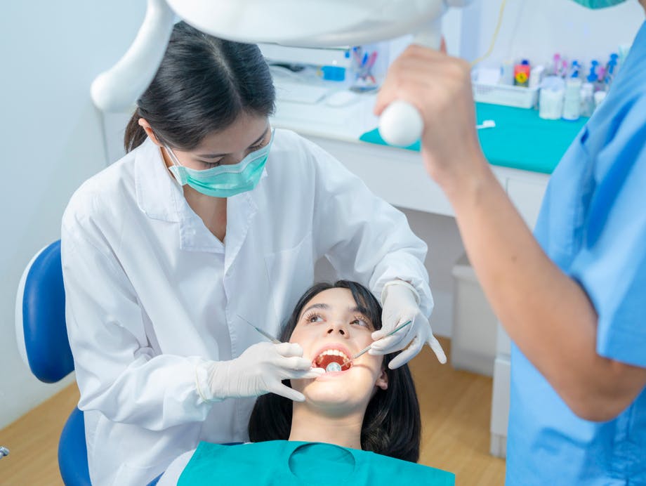 Dentist examines patient while dental hygienist adjusts operatory light over both of them