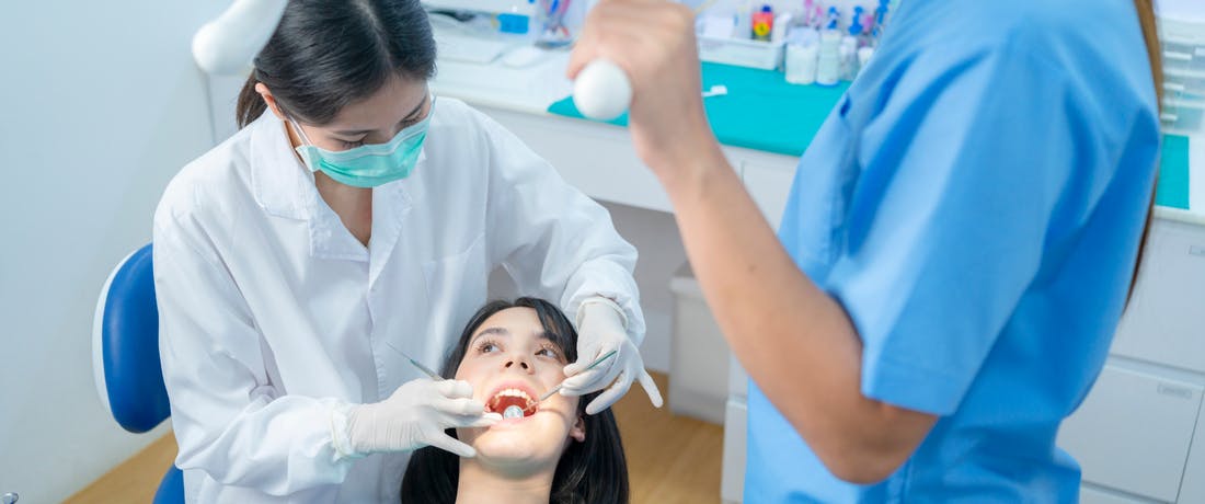 Dentist examines patient while dental hygienist adjusts operatory light over both of them