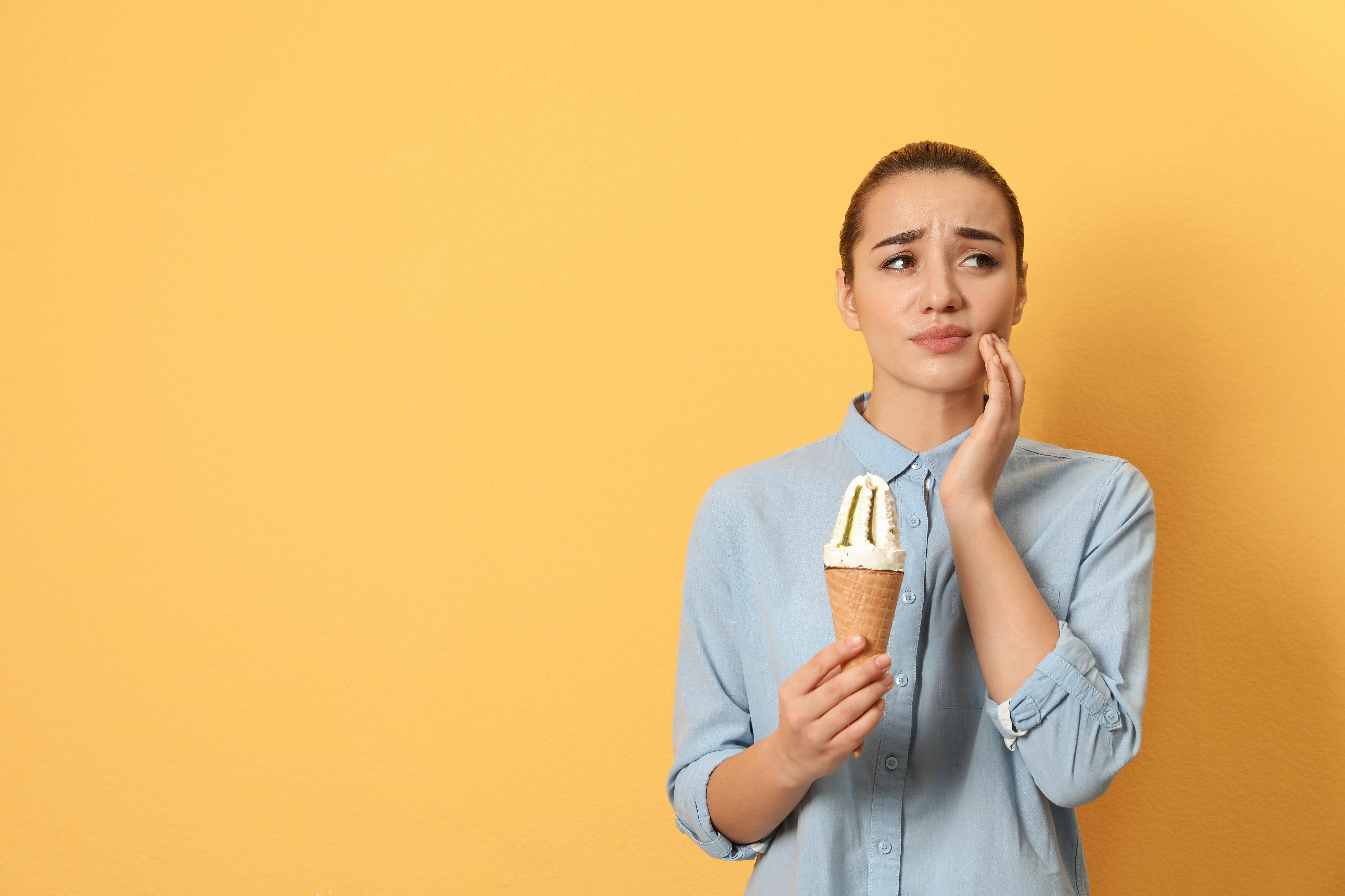 A white woman experiencing sensitive teeth with ice cream