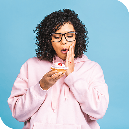 Woman in pink sweatshirt eating cupcake with sensitive teeth