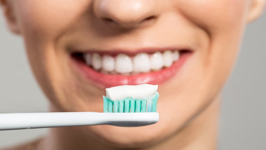Toothpaste on a toothbrush in front of a smiling woman