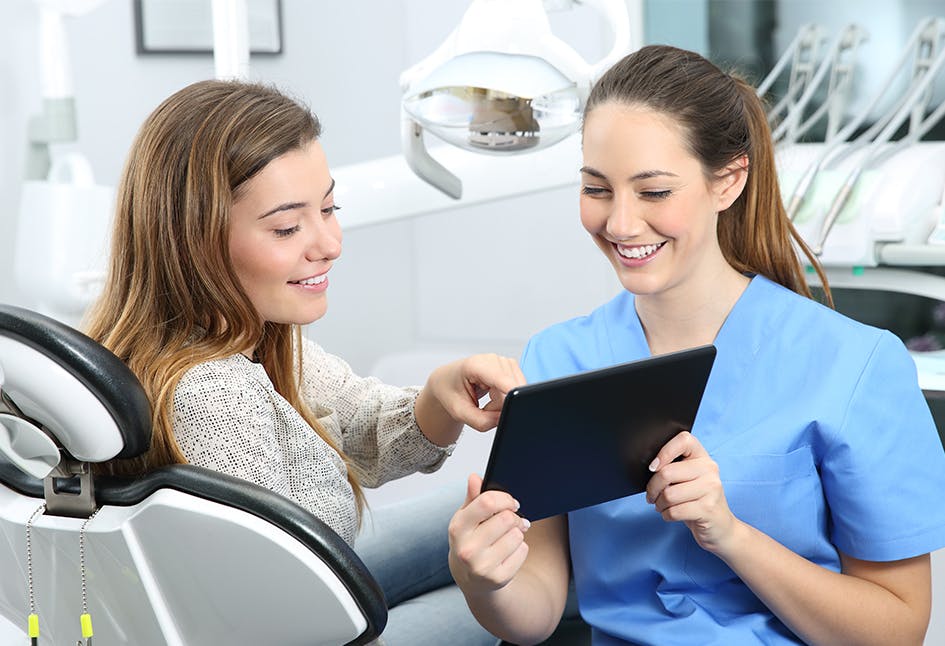 Dentist using a tablet to discuss treatment with a female patient Dentist using a tablet to discuss treatment with a female patient