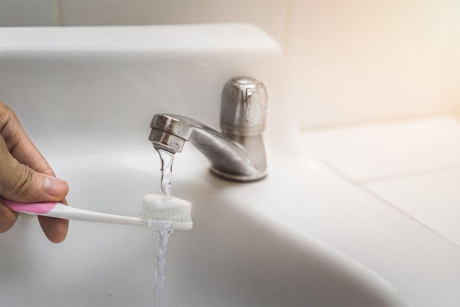 Hand holds a toothbrush with toothpaste under running tap water