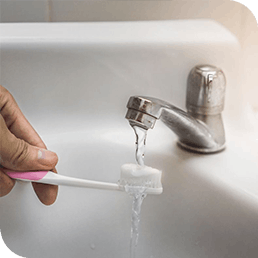 Hand holds a toothbrush with toothpaste under running tap water