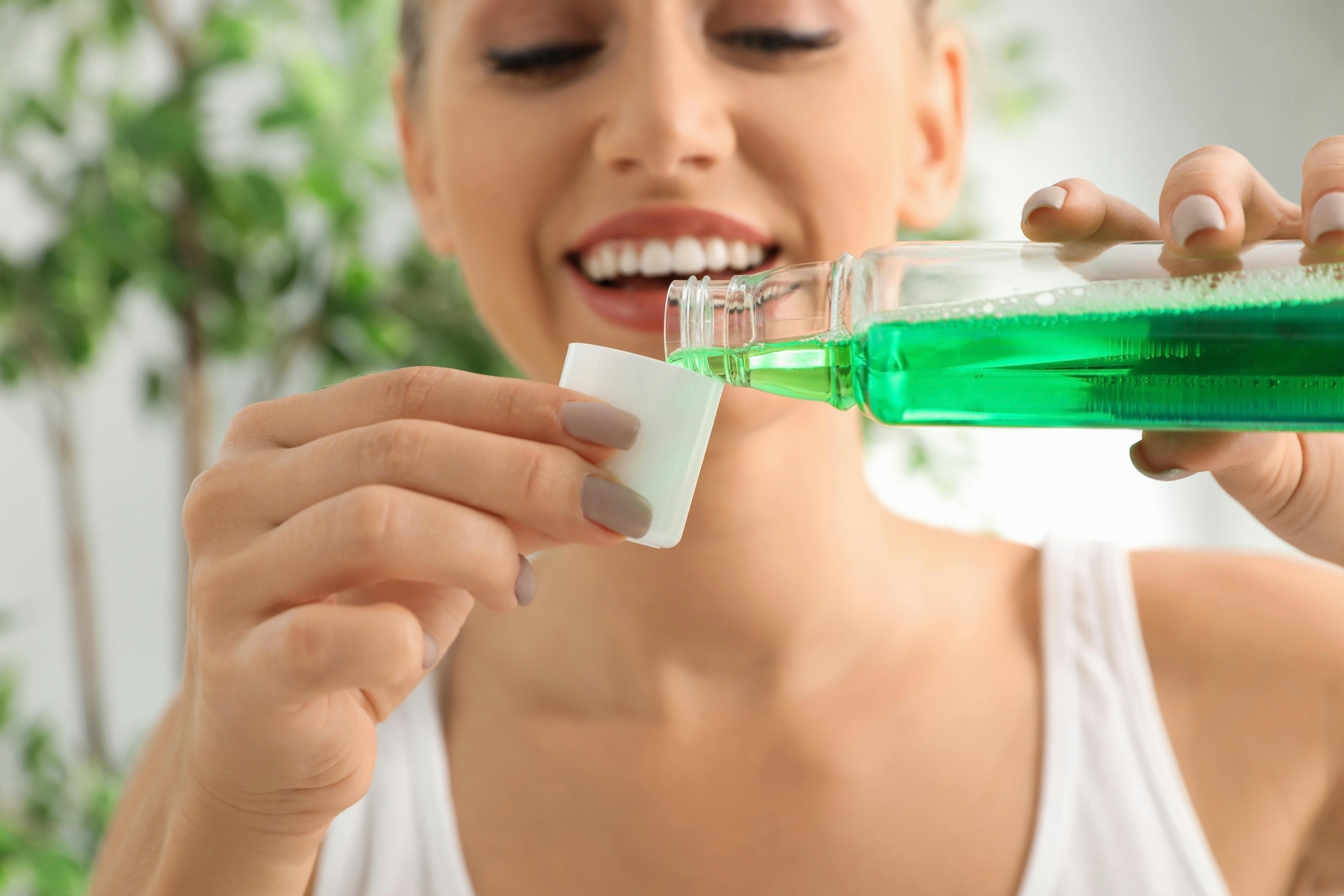 Woman smiles and pours mouthwash into a small cup