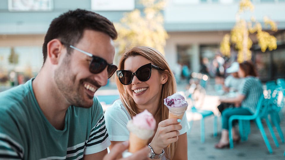 Smiling young couple sitting outdoors and eating ice cream