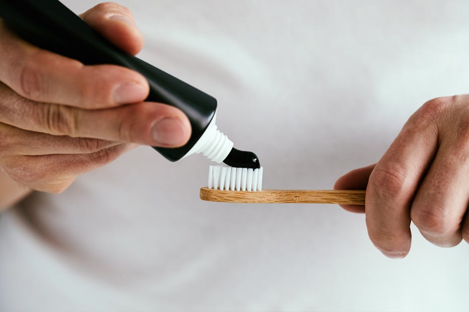 person squeezing black toothpaste on a bamboo toothbrush