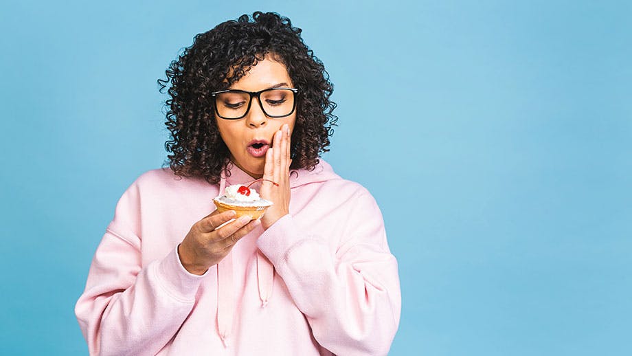 Woman in pink sweatshirt eating cupcake with sensitive teeth