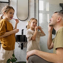 Father helping daughters brush their teeth to remove plaque buildup