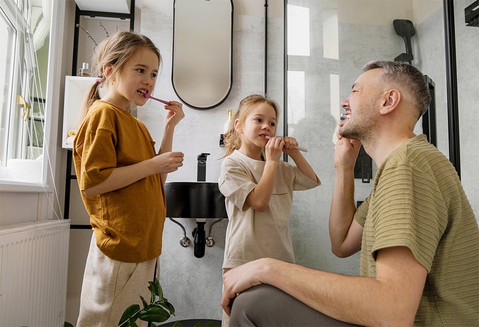 Father helping daughters brush their teeth to remove plaque buildup Father helping daughters brush their teeth to remove plaque buildup