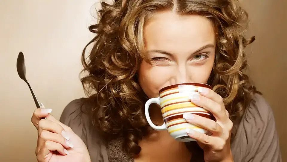 Young woman with curly hair drinks a cup of coffee while winking