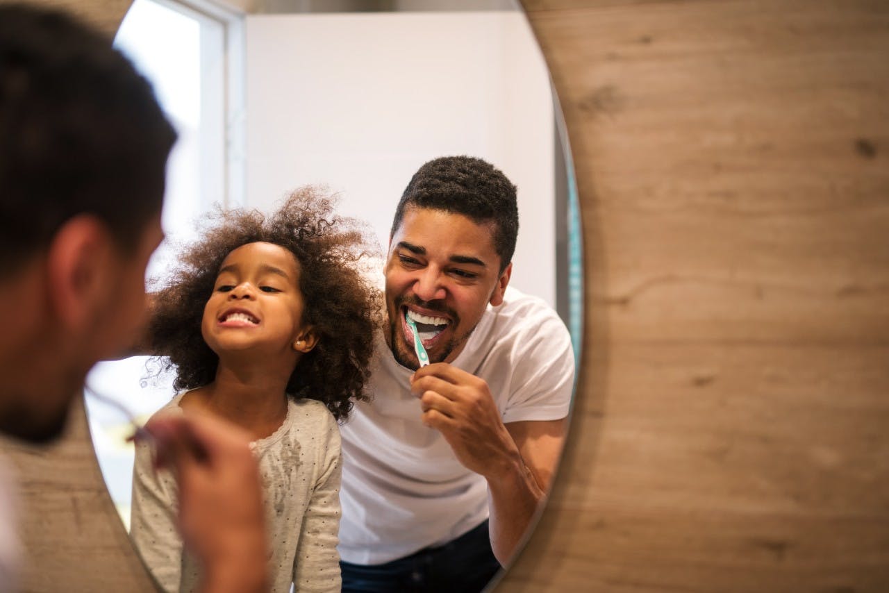 Man smiling and brushing his teeth in the mirror