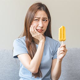 Young woman experiencing cavity pain and cold sensitivity while eating a popsicle.