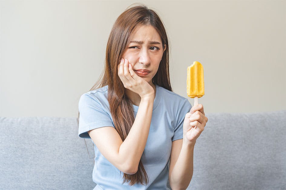 Young woman experiencing cavity pain and cold sensitivity while eating a popsicle.