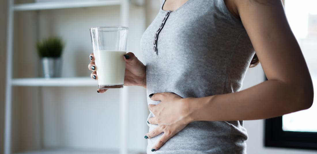 Woman holding glass of milk with right hand and putting her left hand on her stomach