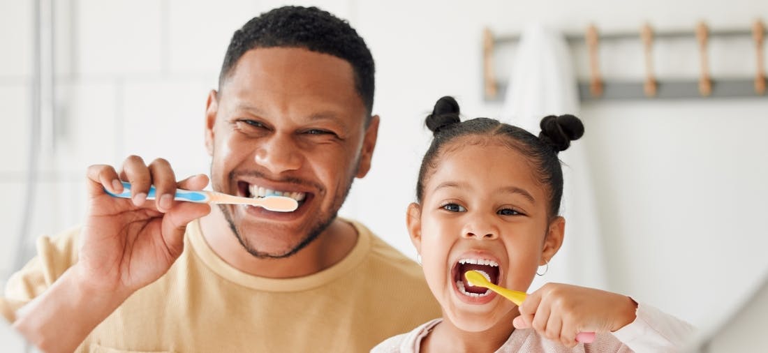 Father and daughter brushing teeth with soft bristle toothbrushes