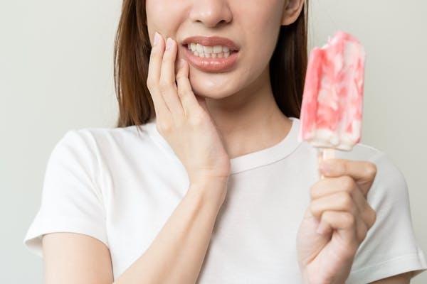 Woman holding hand to mouth and sensitive teeth with popsicle in other hand 