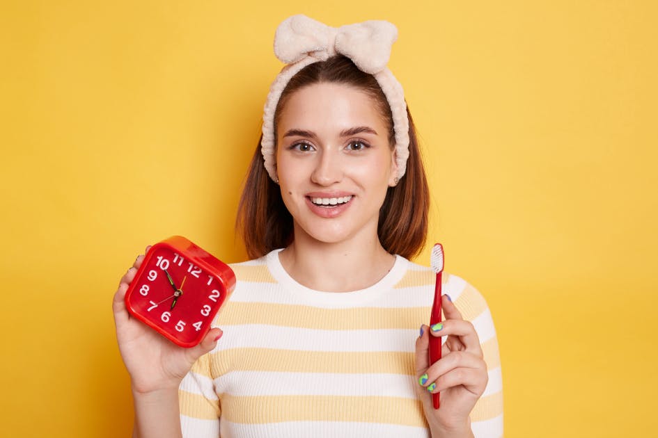 Woman with a pink headband holds a toothbrush and a clock