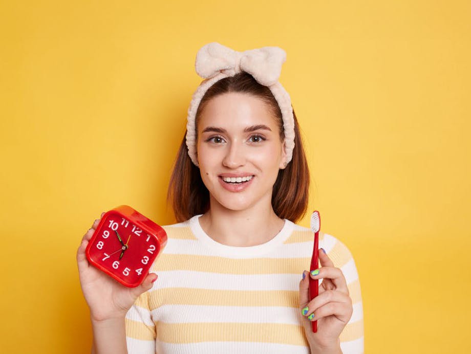 Woman with a pink headband holds a toothbrush and a clock