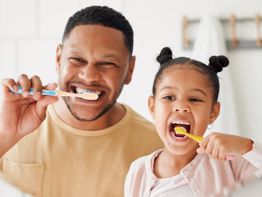 Father and daughter brushing teeth with soft bristle toothbrushes