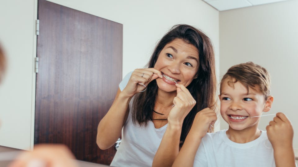 Mother and young son smile in the mirror while flossing teeth.