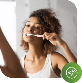 A women brushing her teeth looking in a mirror