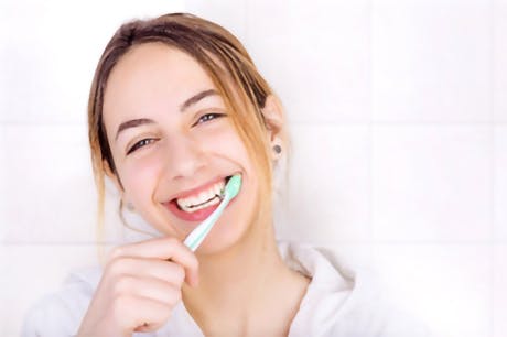 Image of a smiling woman brushing her teeth with a manual toothbrush