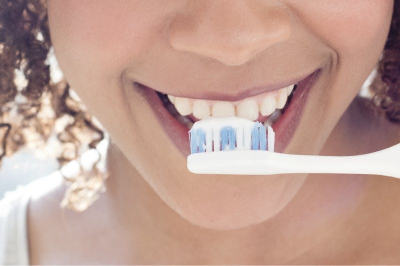 Mulher jovem a escovar os dentes com pasta de dentes Sensodyne para dentes sensíveis