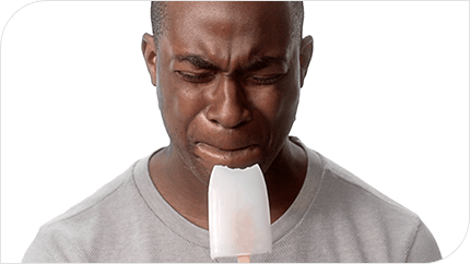 A man biting into an ice lolly showing on his face the pain of having sensitive teeth