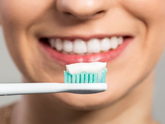 Toothpaste on a toothbrush in front of a smiling woman Toothpaste on a toothbrush in front of a smiling woman