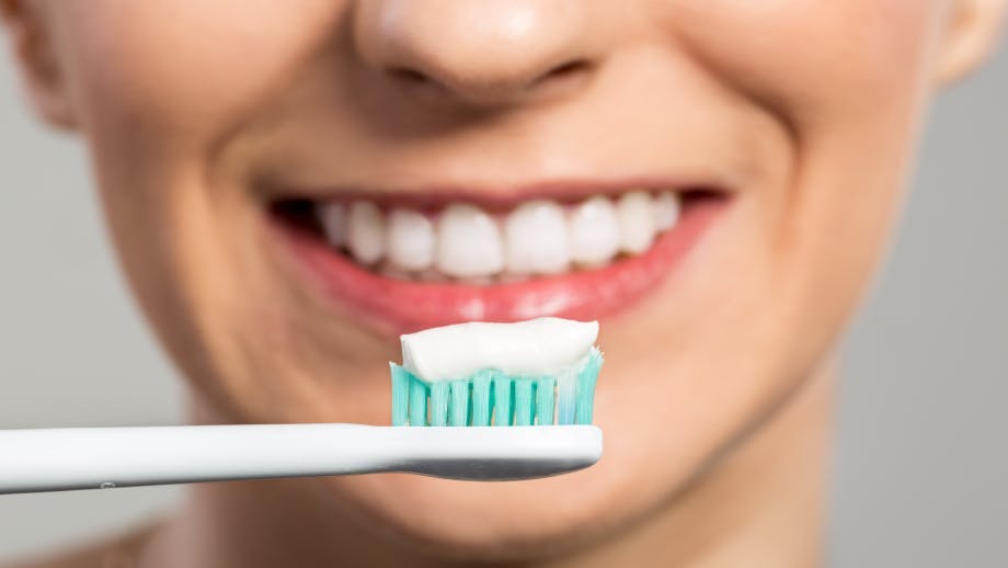 Toothpaste on a toothbrush in front of a smiling woman Toothpaste on a toothbrush in front of a smiling woman