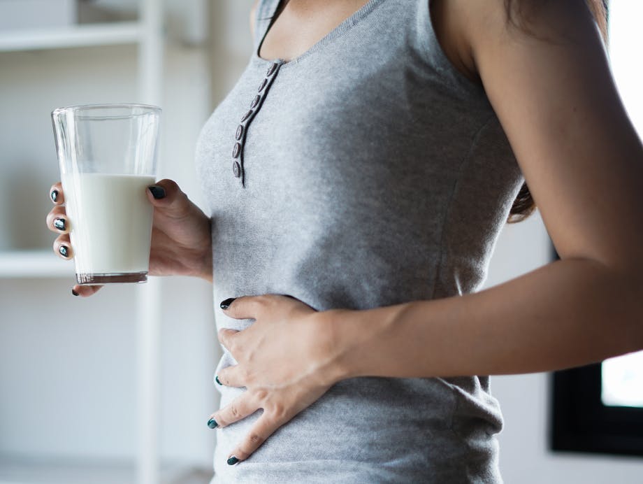 Woman holding glass of milk with right hand and putting her left hand on her stomach Woman holding glass of milk with right hand and putting her left hand on her stomach