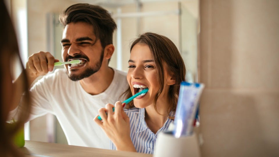 Young couple brushing their teeth together while looking in a mirror Young couple brushing their teeth together while looking in a mirror