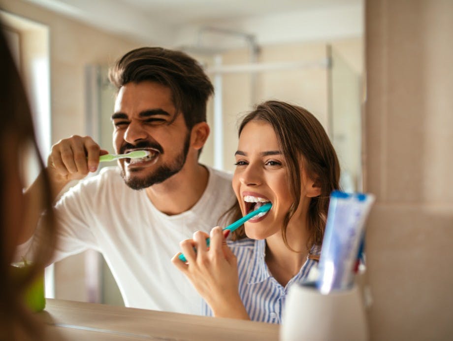 Young couple brushing their teeth together while looking in a mirror Young couple brushing their teeth together while looking in a mirror