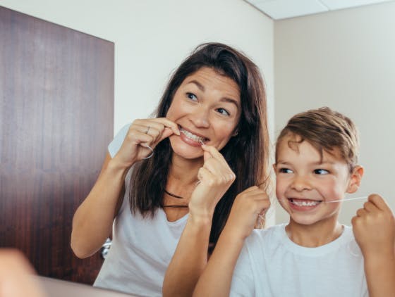Mother and young son smile in the mirror while flossing teeth. Mother and young son smile in the mirror while flossing teeth.